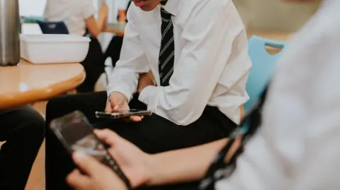 Getty Images Two boys in uniform look at their smartphones sitting at a wooden table