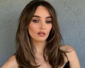 A person with styled hair and makeup facing forward against a plain background