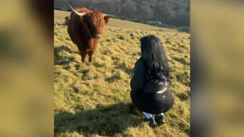 Renata Del Valle Renata Del Valle crouched in front of a highland cow