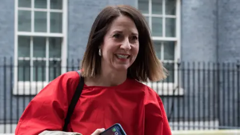 Getty Images Technology Secretary Liz Kendall wearing a red top and holding a mobile phone.