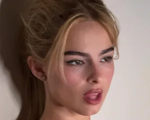 A person with a thoughtful expression hair tied back posing indoors