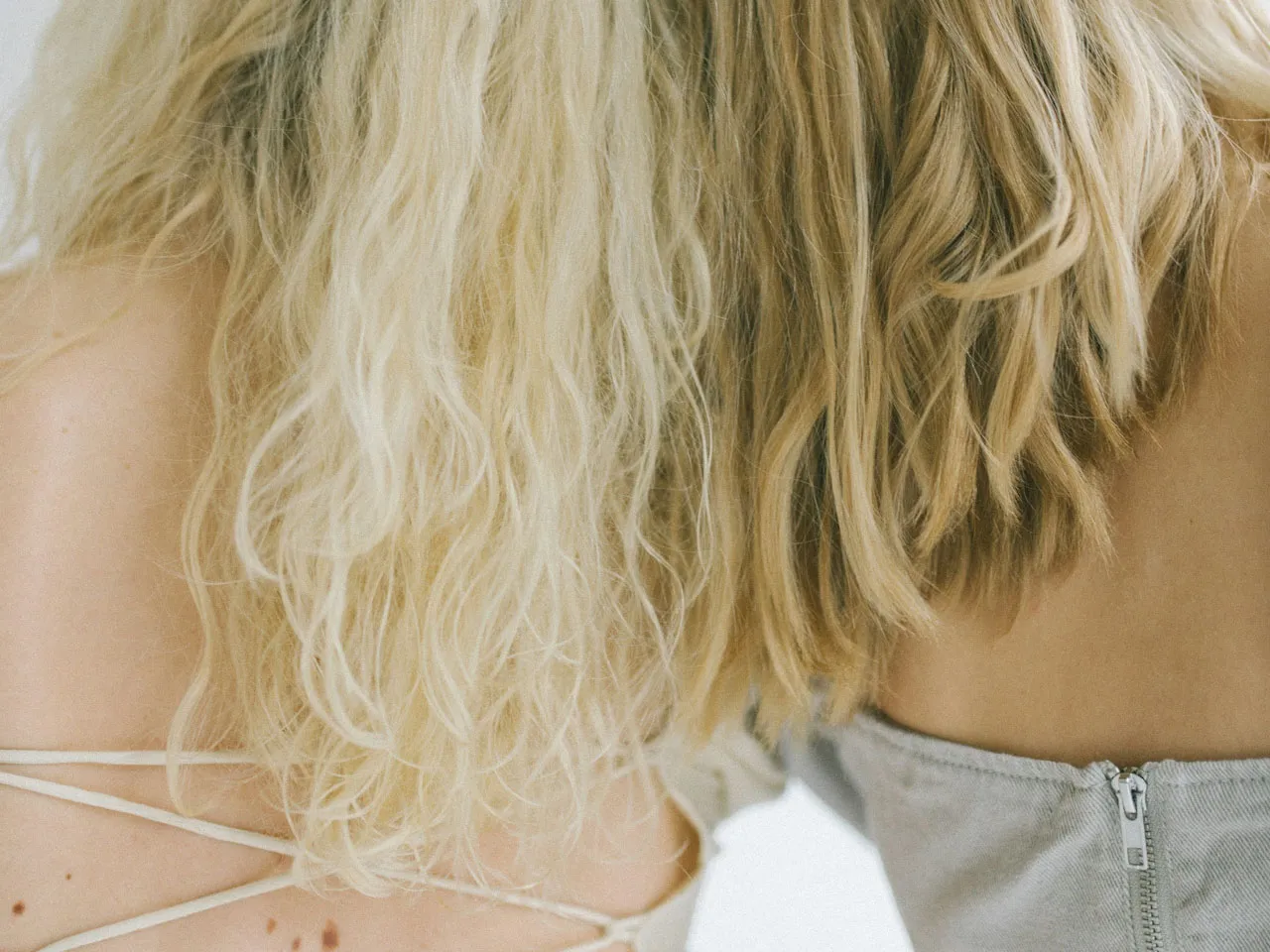 Back view of two individuals with different hair textures wearing strappy and zipped tops