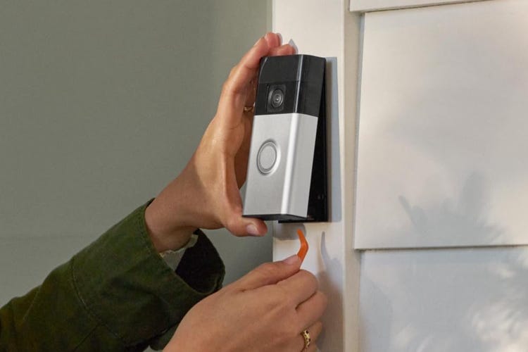 Hands install a Ring video doorbell on white trim.